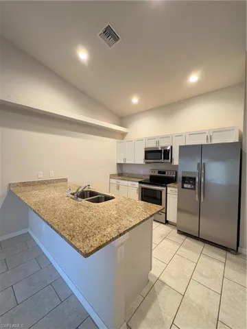 Kitchen featuring kitchen peninsula, stainless steel stove, light tile patterned flooring, white fridge, and white cabinetry