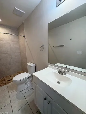 Bathroom featuring tile patterned flooring, vanity, toilet, and tiled shower