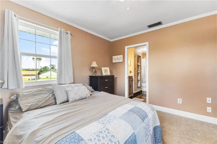 Carpeted bedroom with ornamental molding, ensuite bathroom, and ceiling fan