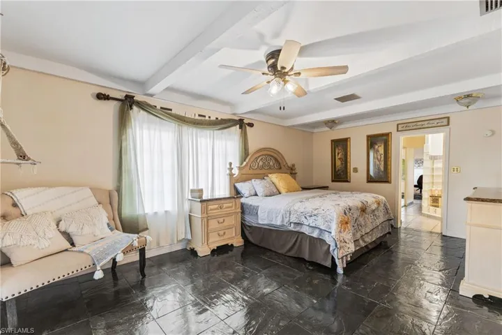 Bedroom featuring ceiling fan, beam ceiling, and ensuite bath