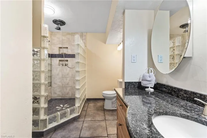 Bathroom with tiled shower, tile patterned flooring, toilet, and vanity
