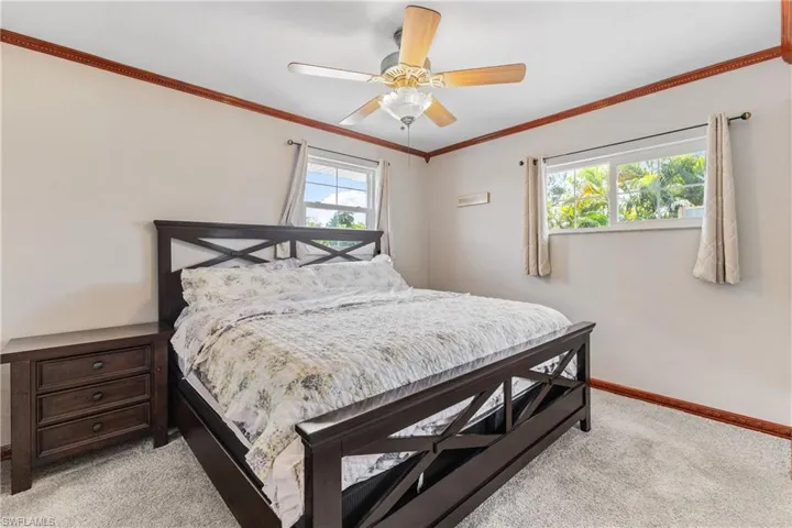 Carpeted bedroom with multiple windows, ceiling fan, and ornamental molding