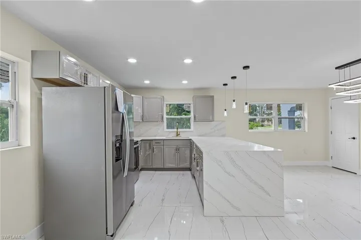 Kitchen with pendant lighting, sink, gray cabinetry, stainless steel fridge, and light stone countertops