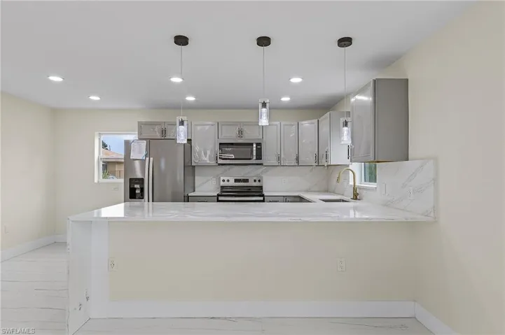 Kitchen with gray cabinets, appliances with stainless steel finishes, tasteful backsplash, sink, and kitchen peninsula