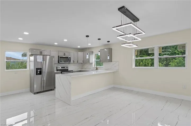Kitchen with gray cabinetry, hanging light fixtures, stainless steel appliances, tasteful backsplash, and kitchen peninsula