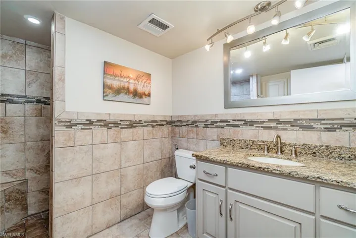 Full bathroom with vanity, light tile patterned floors, tile walls, wainscoting, and a shower