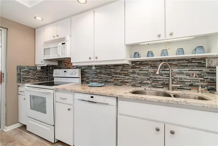 Kitchen with white appliances, open shelves, white cabinetry, light stone counters, and tasteful backsplash