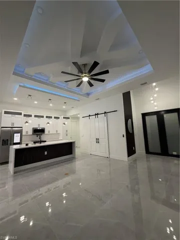 Unfurnished living room with a barn door, a raised ceiling, recessed lighting, and ceiling fan