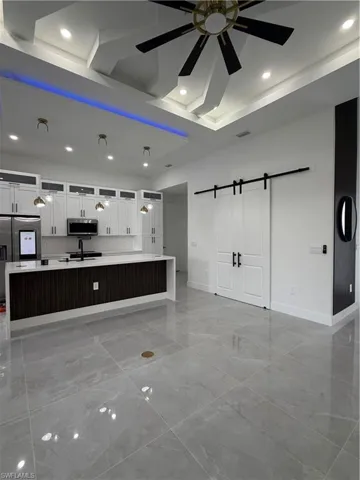 Kitchen with a barn door, white cabinets, a ceiling fan, a large island with sink, and refrigerator