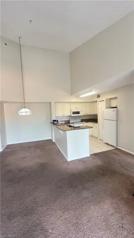 Kitchen with a peninsula, white appliances, light colored carpet, high vaulted ceiling, and a textured ceiling