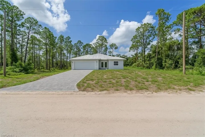 View of front of home with decorative driveway, a front yard, a metal roof, a garage, and view of scattered trees