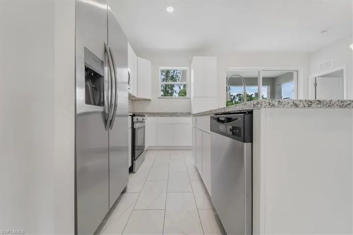 Kitchen with stainless steel appliances, white cabinets, light marble finish floors, light stone countertops, and modern cabinets