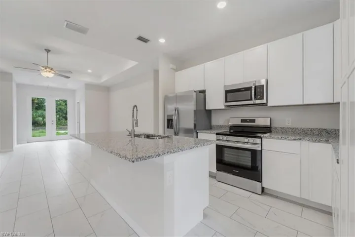 Kitchen featuring stainless steel appliances, light stone countertops, white cabinets, a kitchen island with sink, and recessed lighting