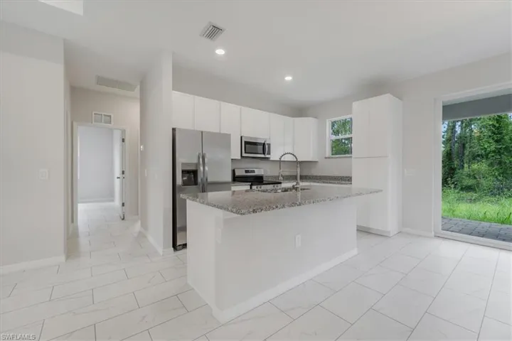 Kitchen with stainless steel appliances, white cabinetry, light stone countertops, a kitchen island with sink, and light marble finish flooring