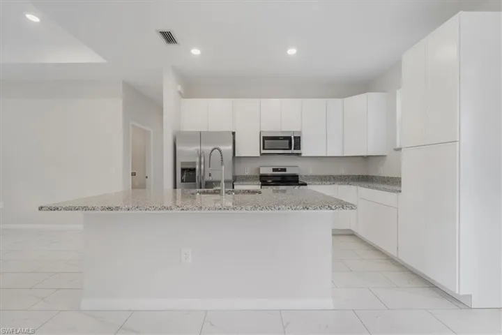 Kitchen featuring white cabinets, stainless steel appliances, light stone countertops, an island with sink, and recessed lighting