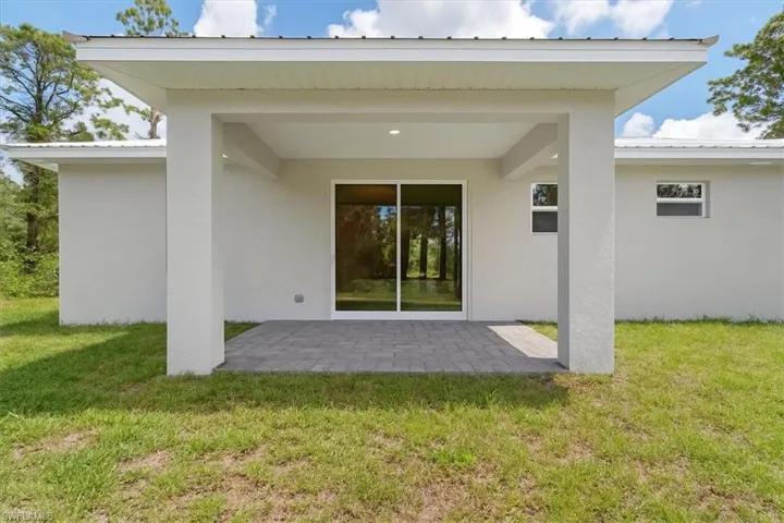 Back of property featuring a metal roof, a patio, stucco siding, and a yard