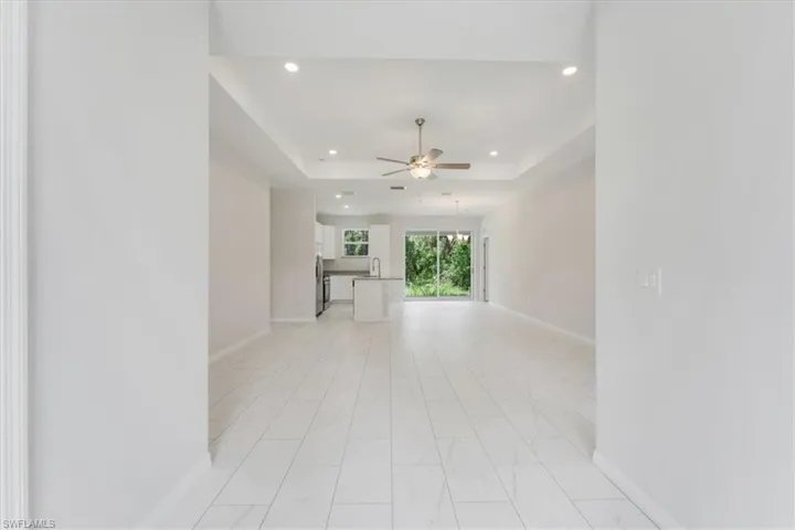 Unfurnished living room with ceiling fan, a tray ceiling, recessed lighting, and light marble finish floors