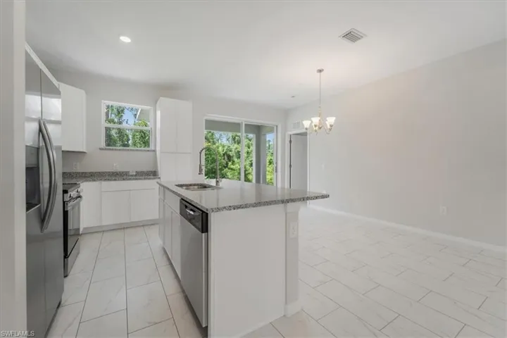 Kitchen with modern cabinets, white cabinetry, stainless steel appliances, light stone countertops, and an island with sink