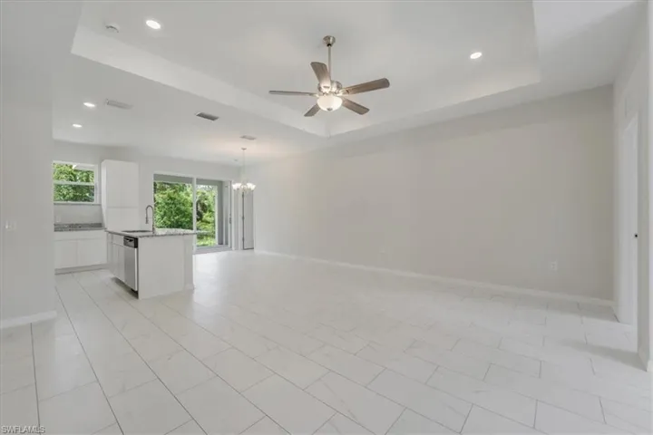Spare room with hanging lights, ceiling fan, light marble finish flooring, and a tray ceiling