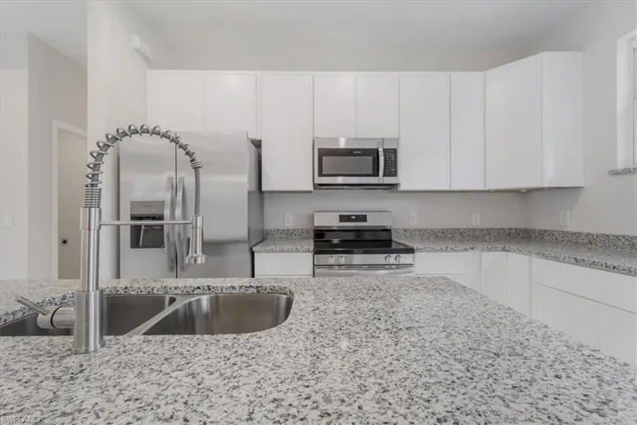 Kitchen with stainless steel appliances, white cabinetry, and light stone counters