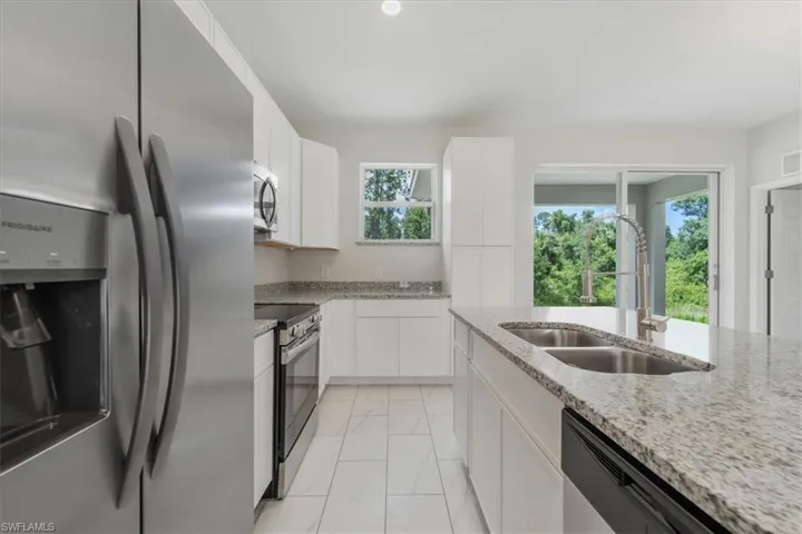 Kitchen with stainless steel appliances, white cabinets, light marble finish floors, and light stone counters