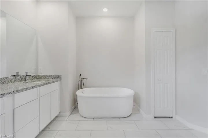 Bathroom featuring a closet, vanity, a soaking tub, light marble finish flooring, and recessed lighting