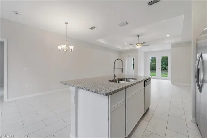 Kitchen featuring white cabinets, light stone countertops, a center island with sink, ceiling fan, and open floor plan