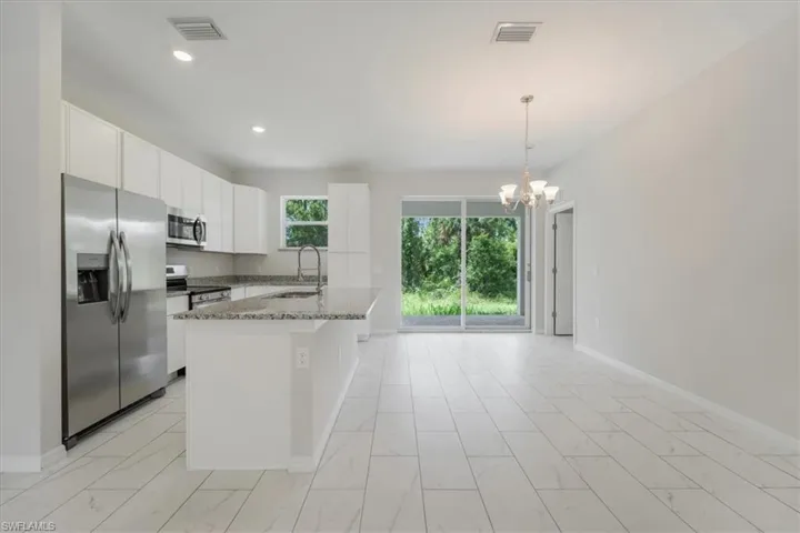 Kitchen featuring stainless steel appliances, light stone counters, white cabinetry, a chandelier, and a kitchen island with sink