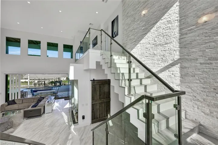 Floating Staircase with solid quartz treads & glass railings seated against a 25' white quartz stack stone accent wall and rock bed