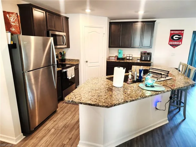 Kitchen with light stone countertops, a center island, light hardwood / wood-style flooring, a breakfast bar area, and appliances with stainless steel finishes
