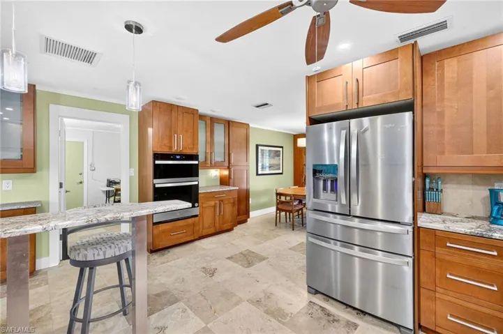 Kitchen featuring brown cabinets, glass insert cabinets, stainless steel appliances, light stone countertops, and recessed lighting