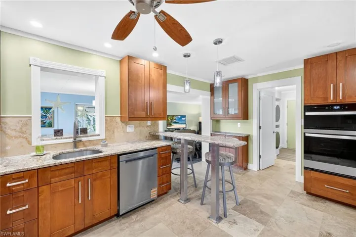 Kitchen featuring brown cabinetry, light stone counters, appliances with stainless steel finishes, glass insert cabinets, and a ceiling fan