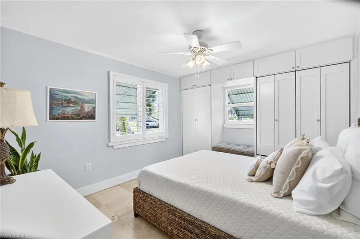 Bedroom with two closets, ornamental molding, multiple windows, a ceiling fan, and light tile patterned floors