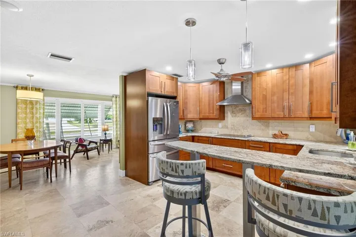 Kitchen featuring light stone counters, brown cabinets, pendant lighting, stainless steel fridge with ice dispenser, and recessed lighting