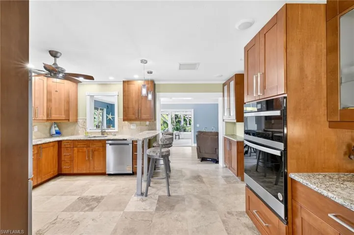 Kitchen featuring brown cabinetry, light stone countertops, double wall oven, decorative backsplash, and dishwasher