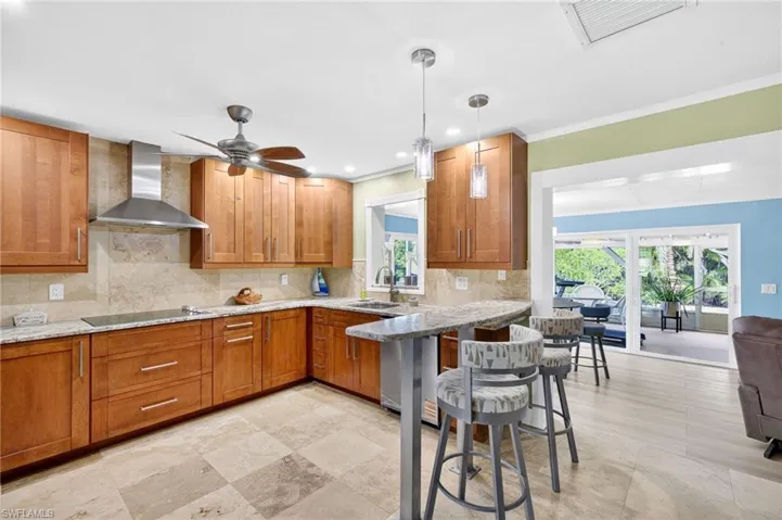 Kitchen with brown cabinets, tasteful backsplash, light stone countertops, a kitchen breakfast bar, and recessed lighting