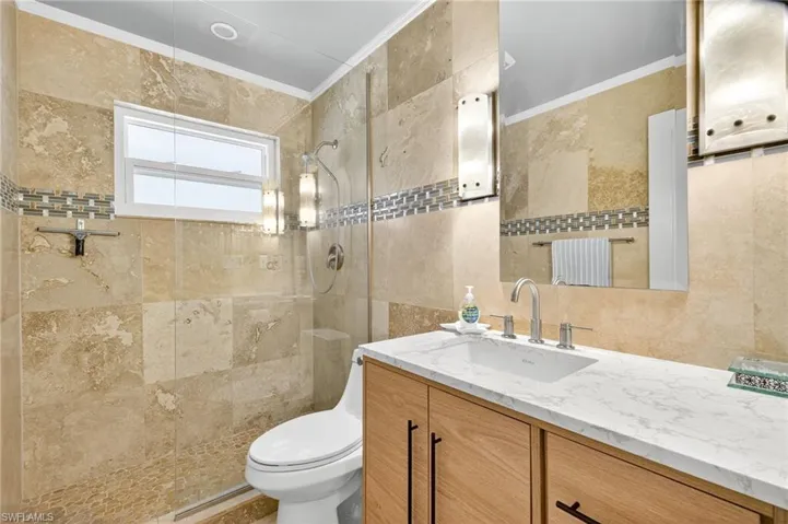 Bathroom featuring vanity, walk in shower, tile walls, and crown molding