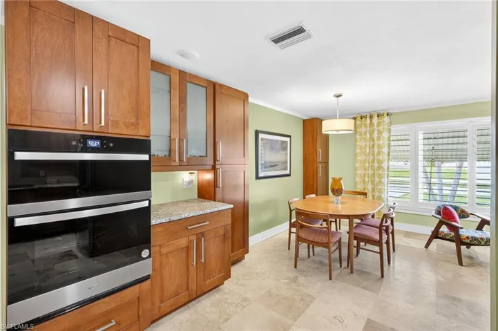 Kitchen with stainless steel double oven, brown cabinets, light stone countertops, crown molding, and hanging light fixtures