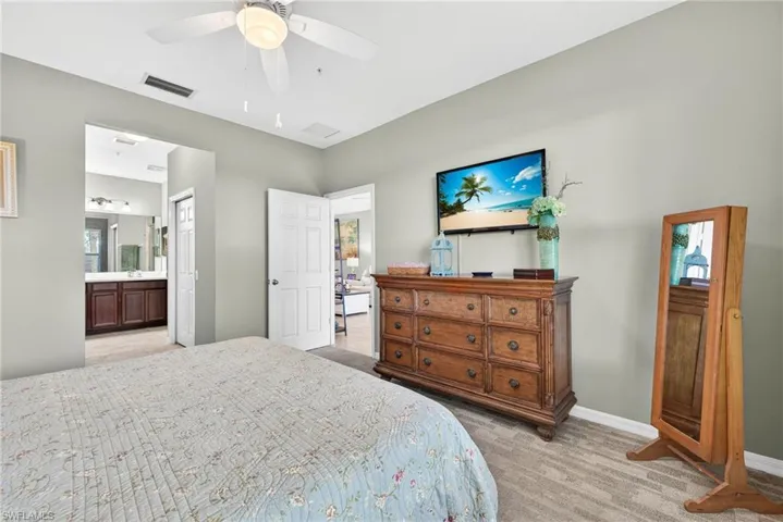 Bedroom with light colored carpet, ceiling fan, and ensuite bathroom