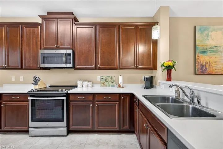 Kitchen with stainless steel appliances, light countertops, decorative light fixtures, and light tile patterned flooring