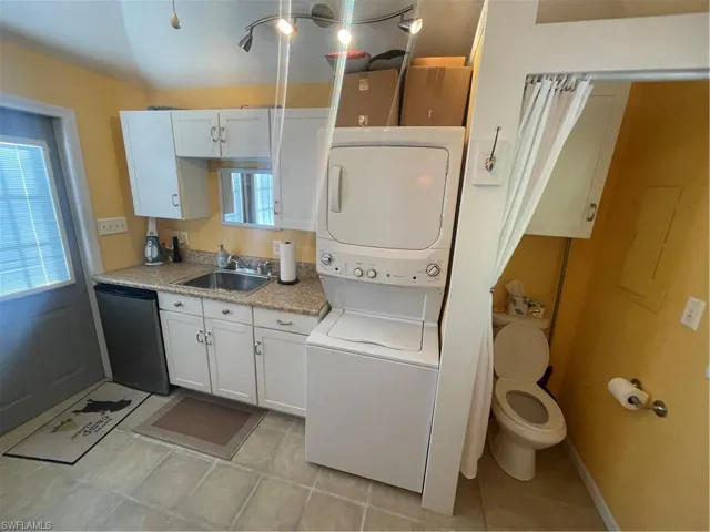 Laundry area with stacked washing machine and dryer and light tile patterned flooring