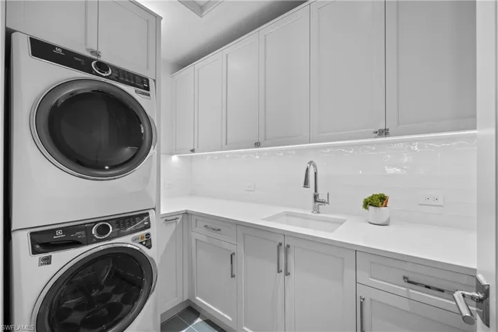 Laundry area with cabinets, sink, light tile patterned floors, and stacked washer and clothes dryer
