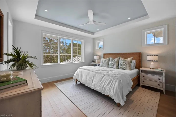 Bedroom with a raised ceiling, ceiling fan, and wood-type flooring