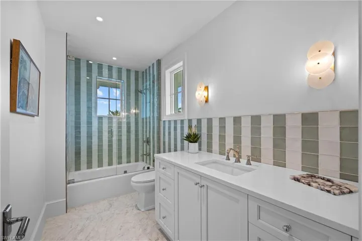Full bathroom with tile walls, enclosed tub / shower combo, vanity, and toilet