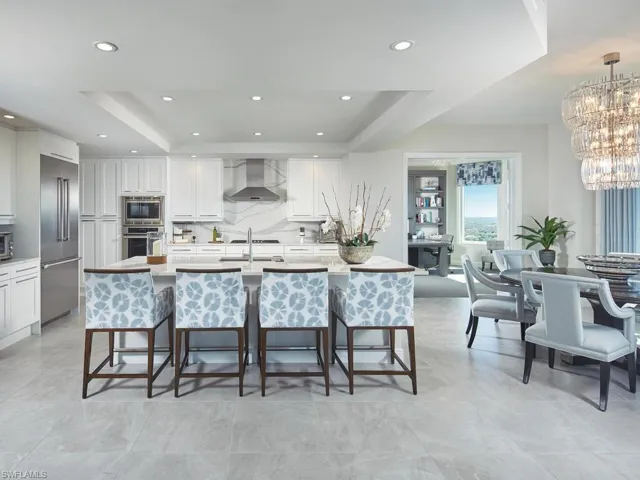 Kitchen with wall chimney range hood, built in appliances, pendant lighting, a tray ceiling, and white cabinets