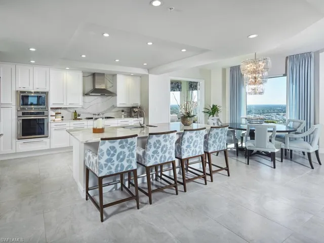 Kitchen featuring a breakfast bar, a kitchen island with sink, a raised ceiling, wall chimney exhaust hood, and stainless steel appliances