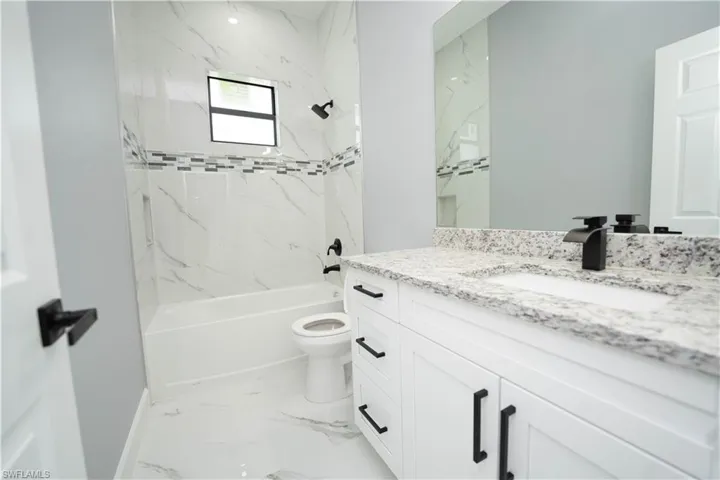 Full bathroom featuring vanity, tiled shower / bath combo, and toilet