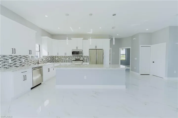Kitchen with pendant lighting, white cabinetry, stainless steel appliances, and a center island