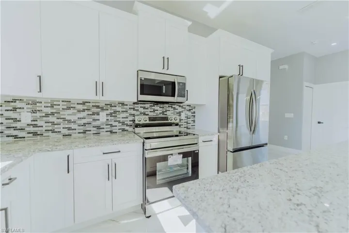 Kitchen featuring stainless steel appliances, white cabinetry, light stone countertops, and tasteful backsplash