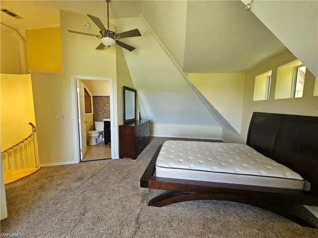 Unfurnished bedroom featuring ceiling fan, carpet floors, lofted ceiling, and ensuite bathroom
